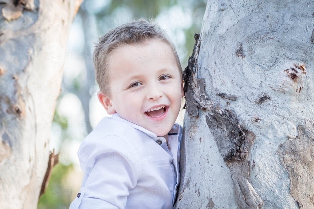 Young caucasian boy leaning against tree laughing - Australian Stock Image