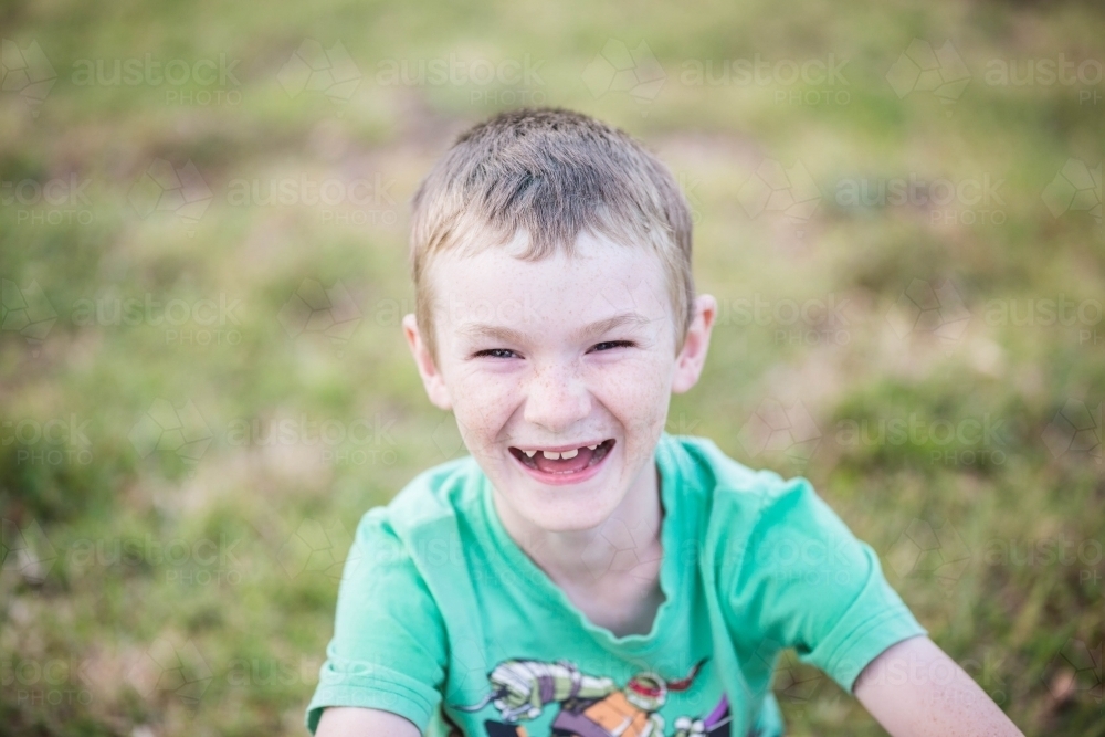Young caucasian boy sitting on grass laughing - Australian Stock Image