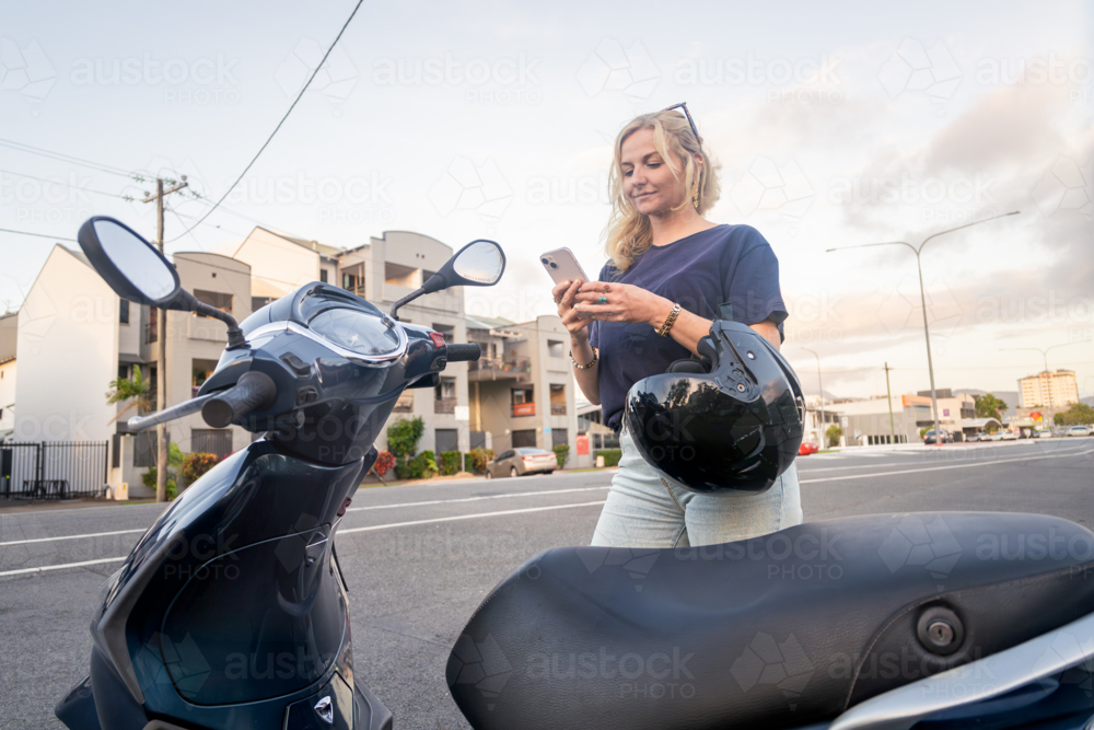 Young Caucasian woman checking her phone before riding her scooter - Australian Stock Image