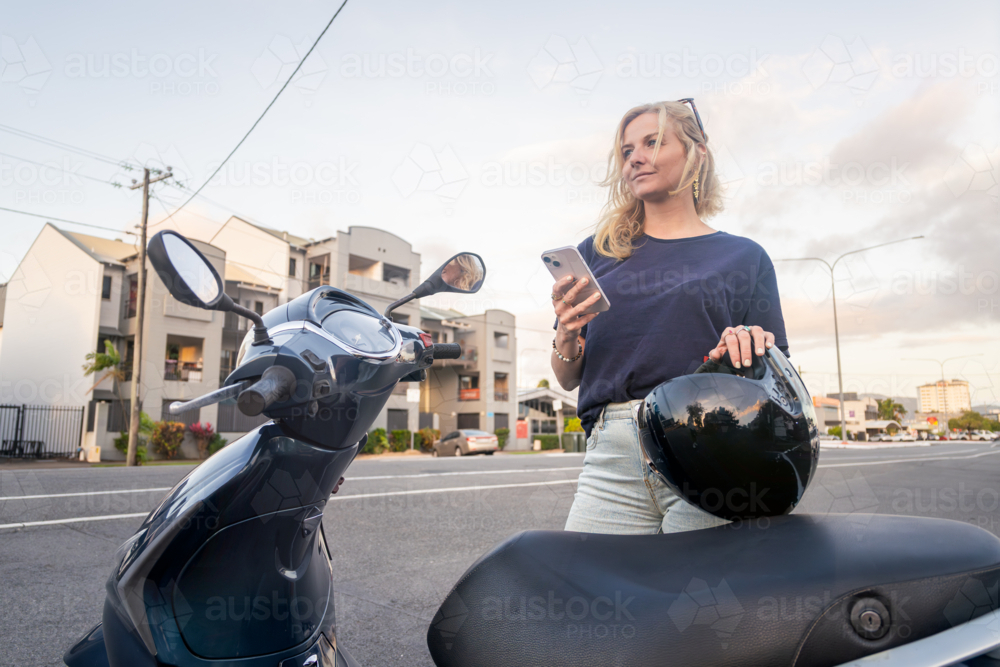 Young Caucasian woman holding her phone before riding her scooter - Australian Stock Image
