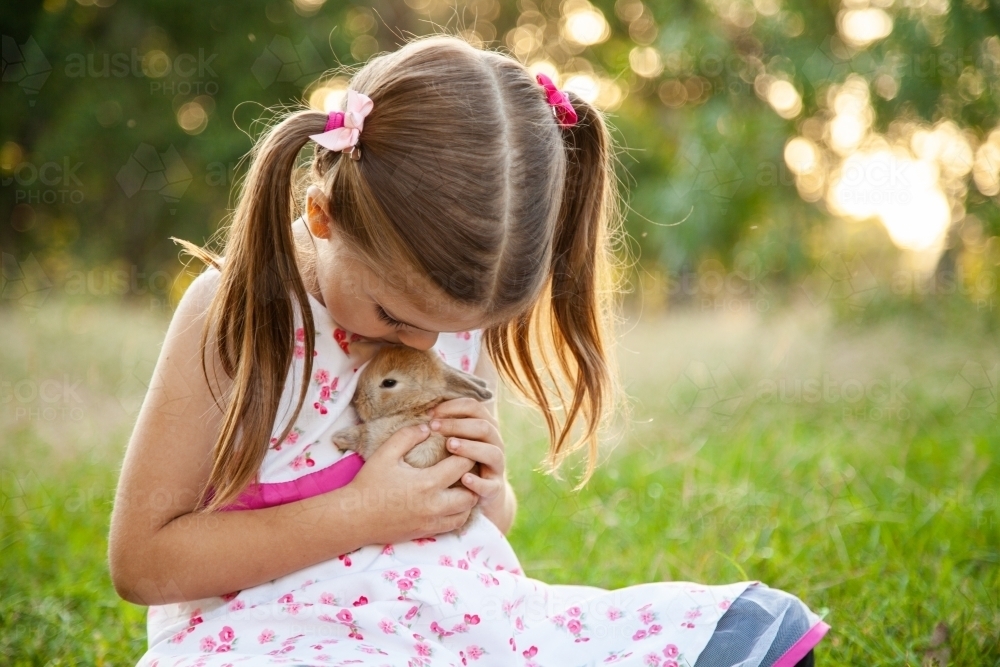 Young child cuddling tiny baby bunny outside - Australian Stock Image