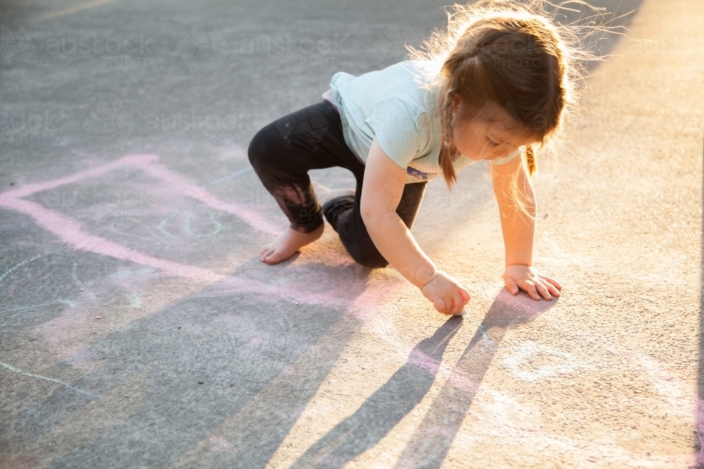 Image of Young child drawing on concrete with coloured chalk in the