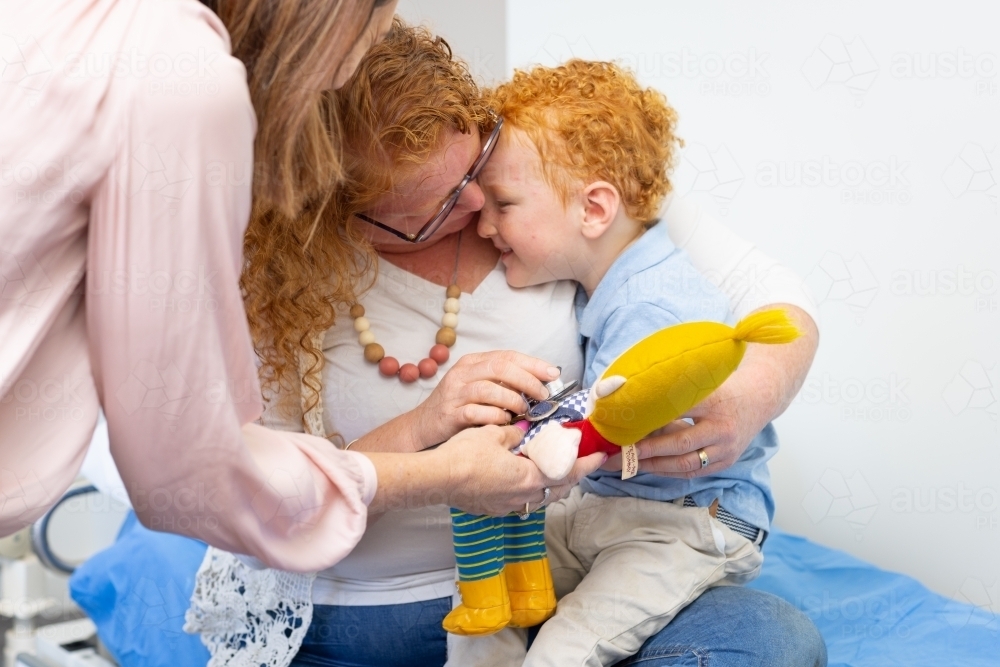young child hiding face in mother's neck at doctor's surgery - Australian Stock Image
