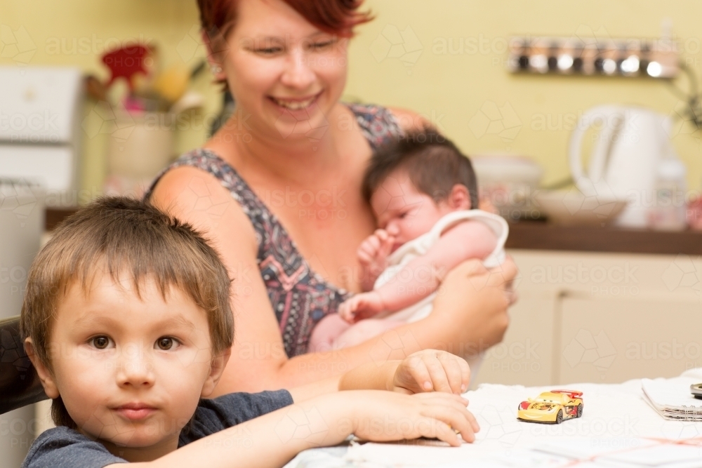 Young child in kitchen with mother and baby - Australian Stock Image