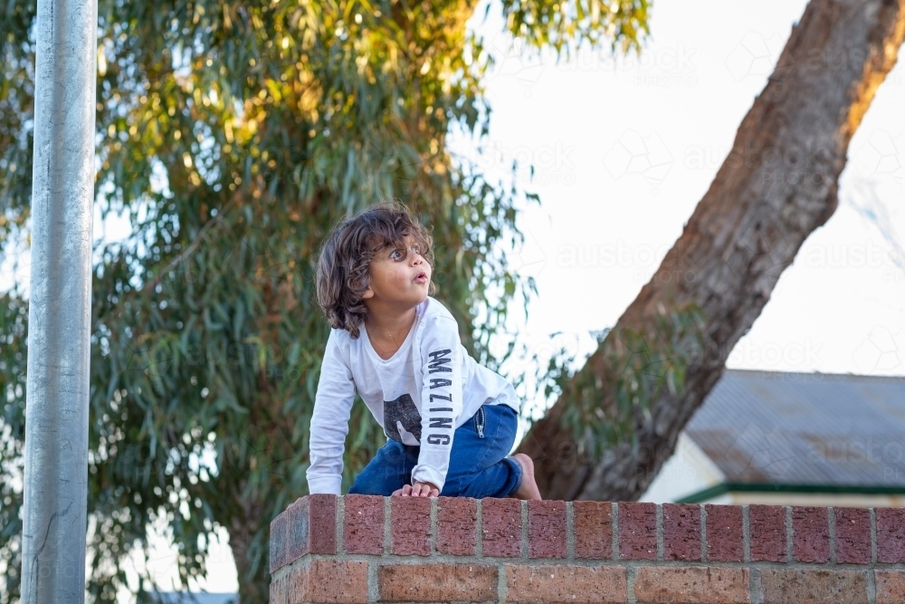 Young child kneeling on brick wall - Australian Stock Image