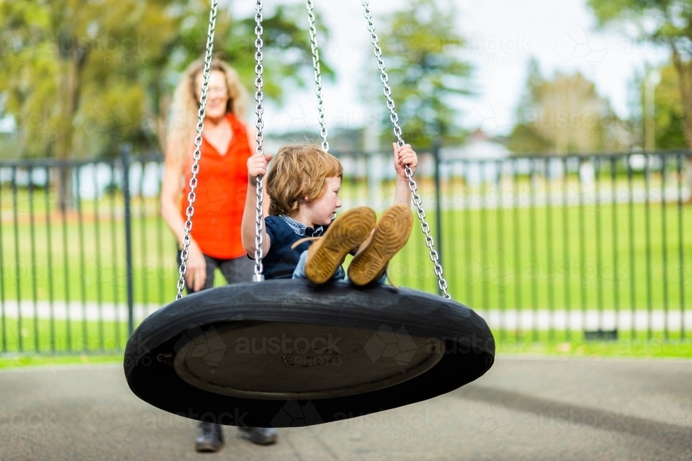 Image of Young child on swing at park with carer Austockphoto