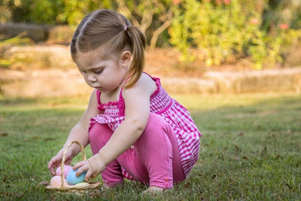 Young child placing Easter eggs in a basket on the lawn - Australian Stock Image