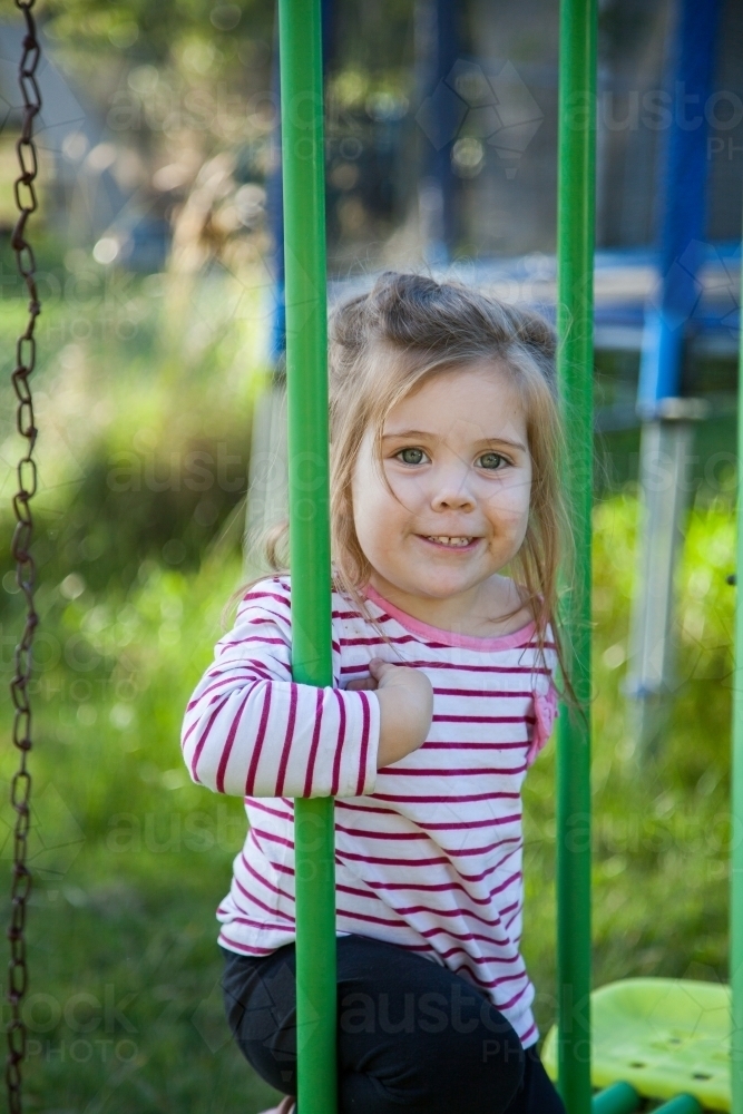 Young child playing on swing on swingset in the backyard - Australian Stock Image