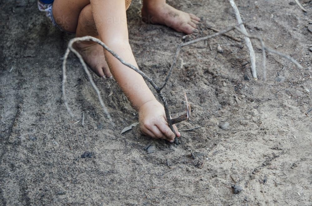 Young child playing with sticks in sandy grey dirt - Australian Stock Image