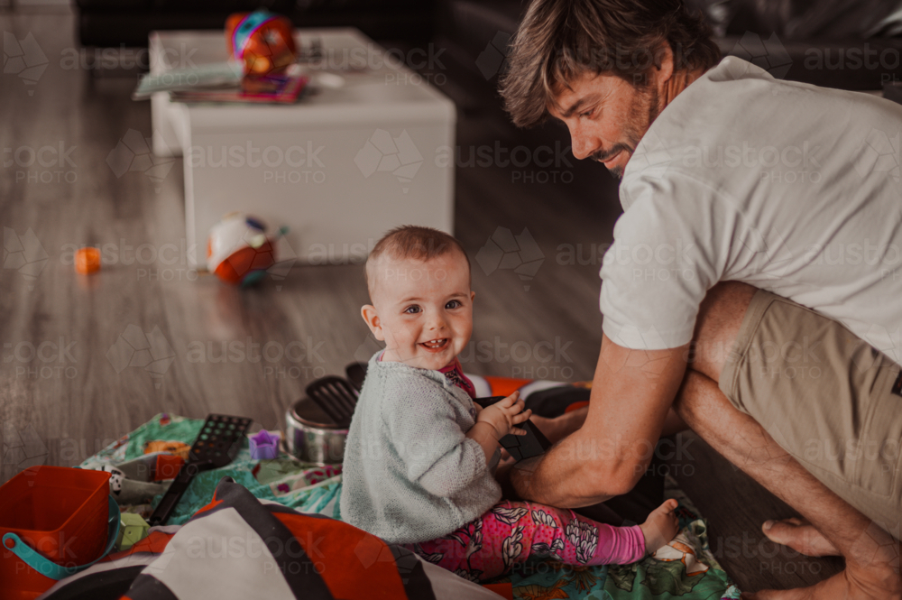 young child playing with toys and pots on the living room alongside a young male father - Australian Stock Image
