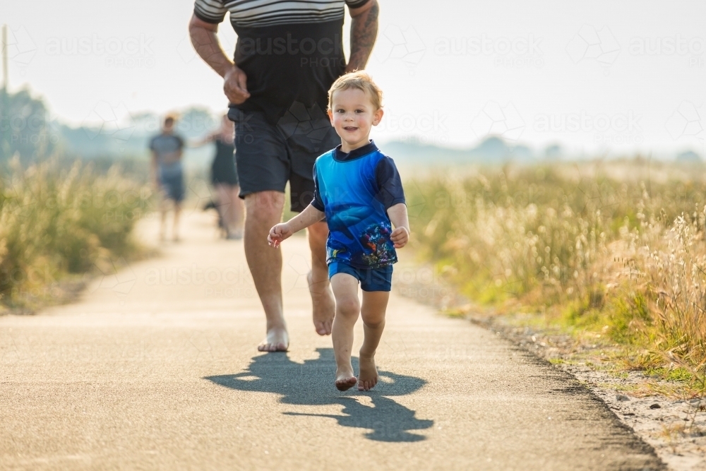 Young child running away from father on path - Australian Stock Image
