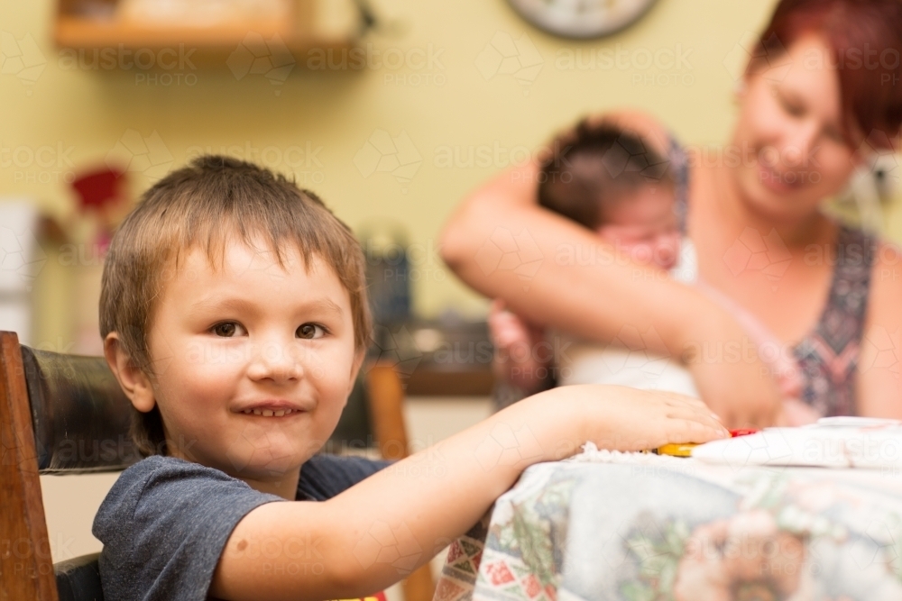Young child sitting at table with mother and baby in background - Australian Stock Image