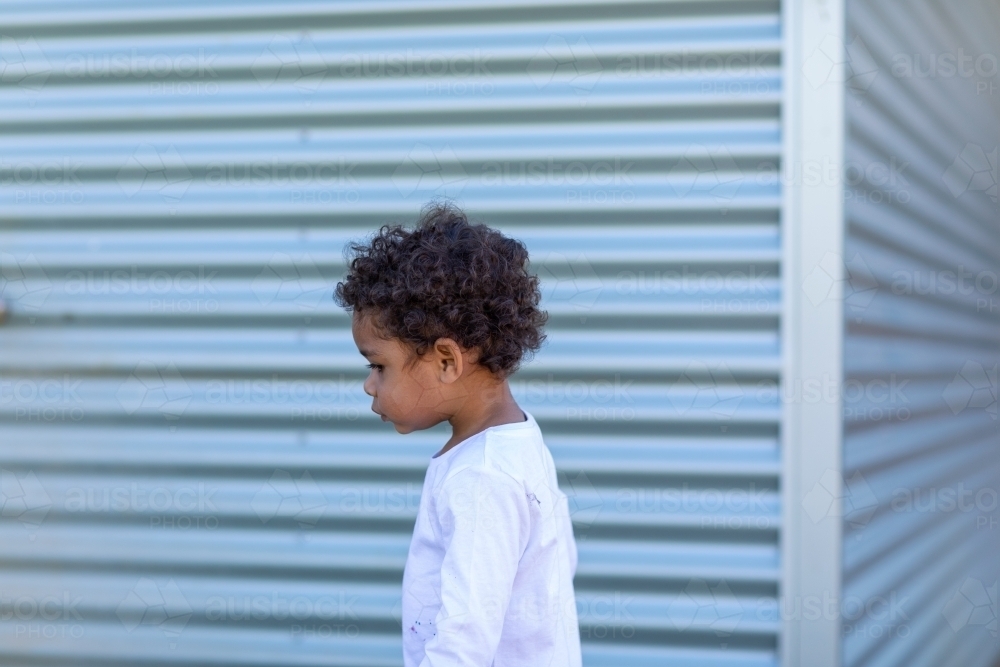 young child walking in front of corrugated iron wall - Australian Stock Image