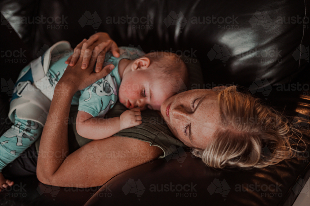 young child wearing a harness while sleeping over mother's chest while mother is sleeping - Australian Stock Image