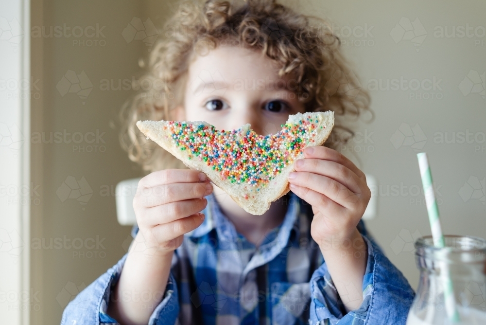 Young child with curly hair holding up a slice of fairy bread - Australian Stock Image