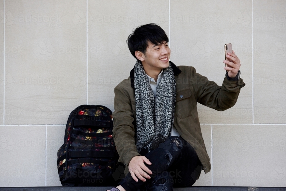 Young Chinese man sitting on bench using mobile phone - Australian Stock Image