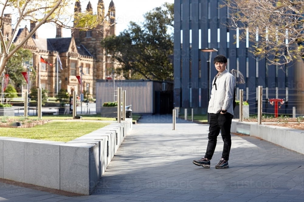 Young Chinese man smiling with backpack at university campus - Australian Stock Image
