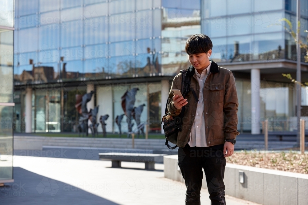 Young Chinese student outdoors checking mobile phone - Australian Stock Image