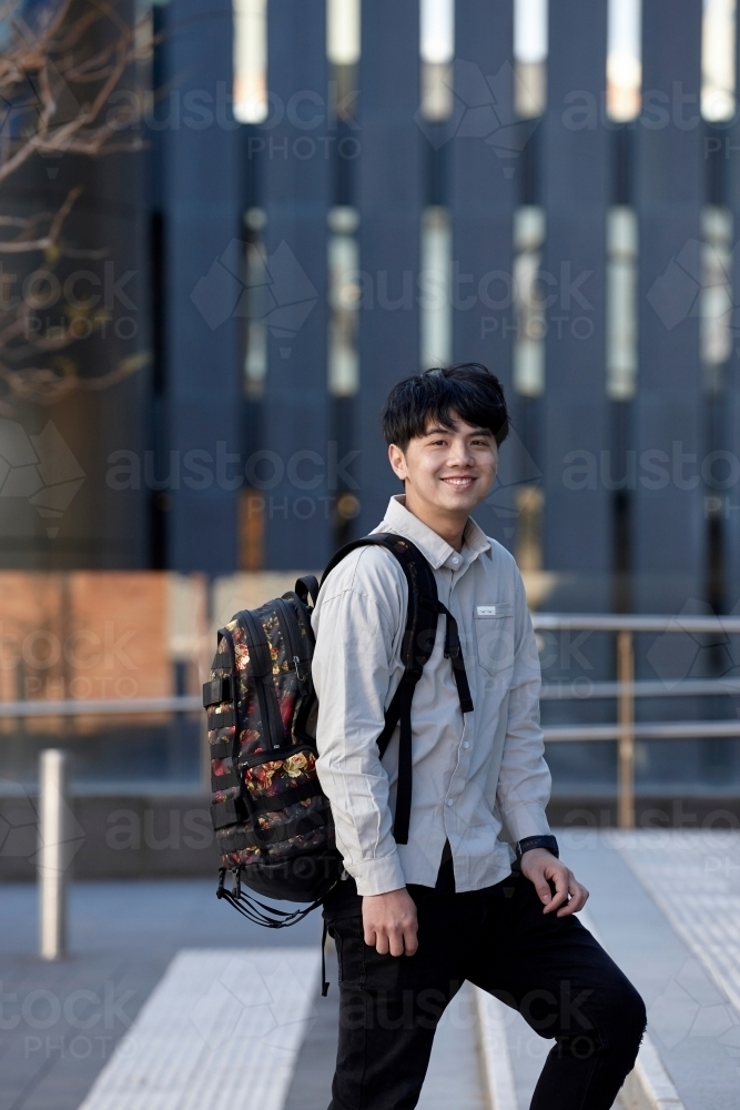 Young Chinese student standing on stairs smiling with buildings behind - Australian Stock Image