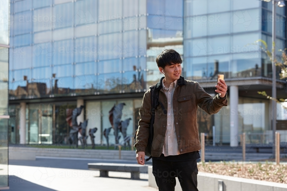 Young Chinese university student standing taking a selfie on-campus - Australian Stock Image
