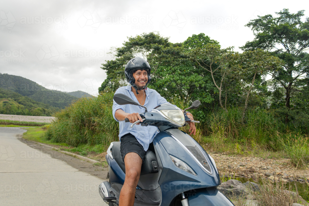 Young Cook Islander man riding a motorbike alone on a rural road in Far North Queensland - Australian Stock Image