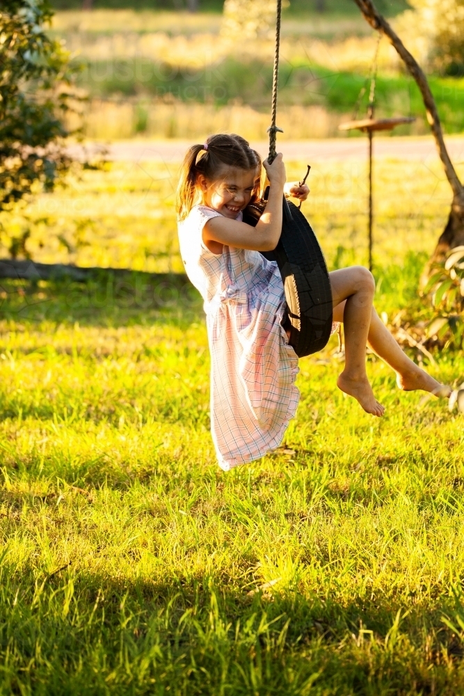 Young country girl playing alone outdoors on tyre swing - Australian Stock Image
