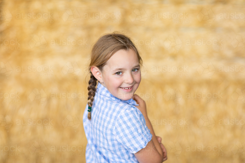 young country girl wearing blue checked shirt looking over her shoulder with blurry background - Australian Stock Image