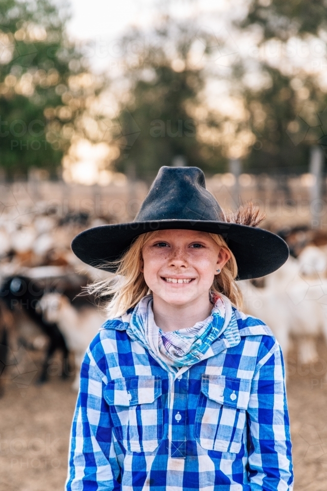Young country girl wearing, hat, scarf and checkered shirt with goats in the background - Australian Stock Image
