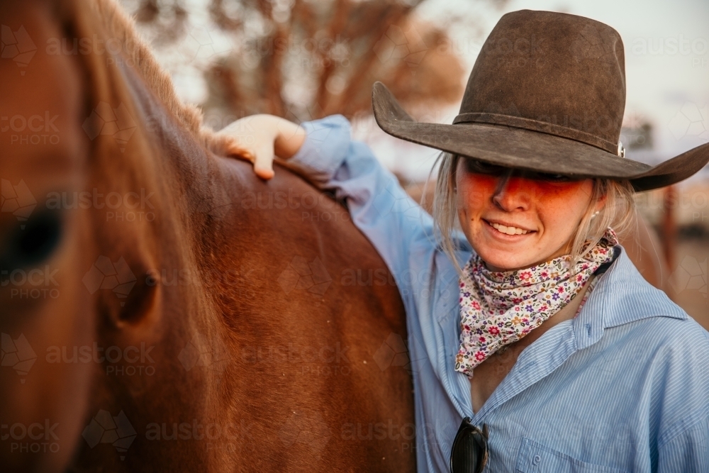 Young country woman with a brown hat leaning on horse - Australian Stock Image