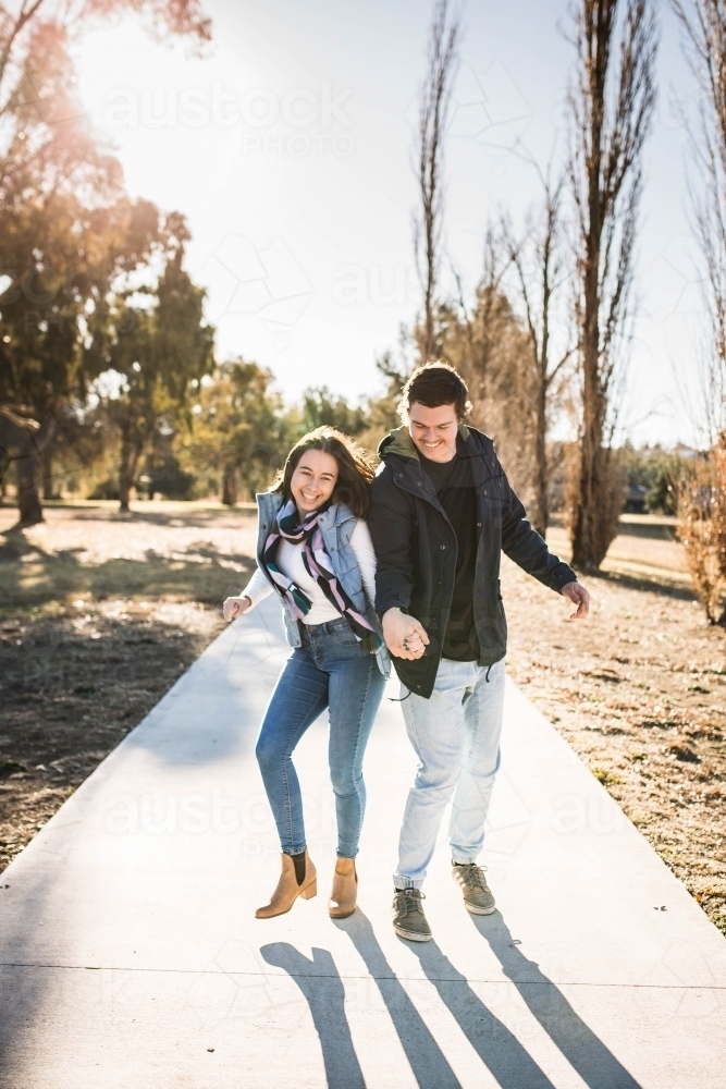 Young couple holding hands dancing on footpath laughing - Australian Stock Image
