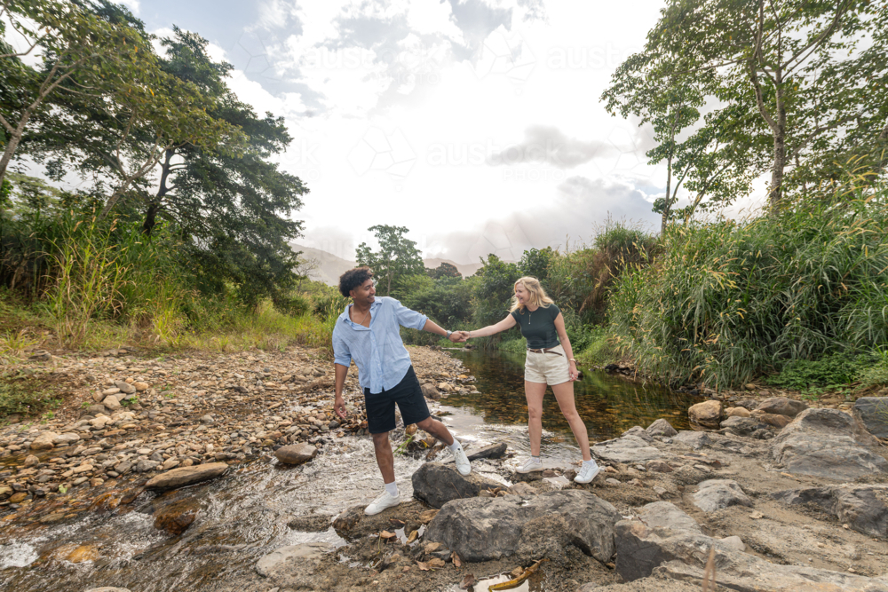 Young couple holding hands exploring a creek in far north Queensland - Australian Stock Image