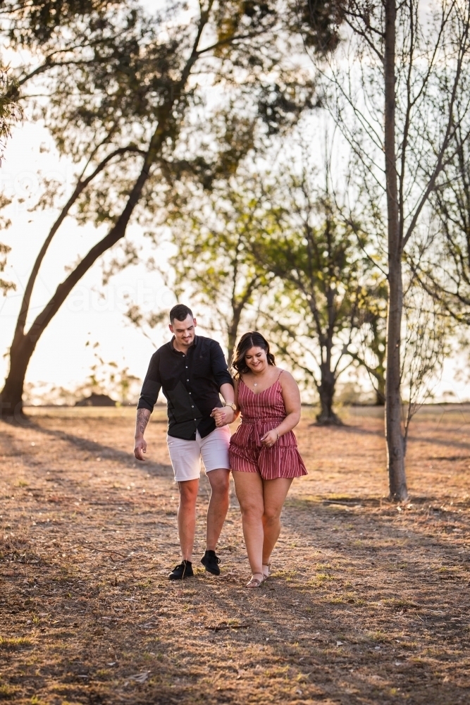 Young couple holding hands laughing walking - Australian Stock Image