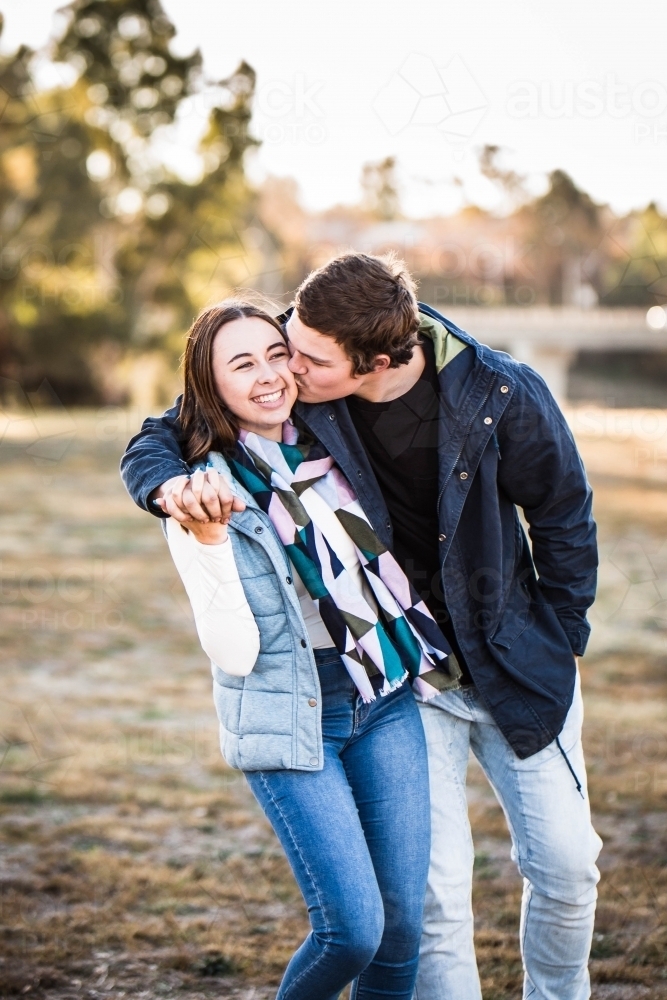 Young couple holding hands walking while man kisses woman on cheek - Australian Stock Image