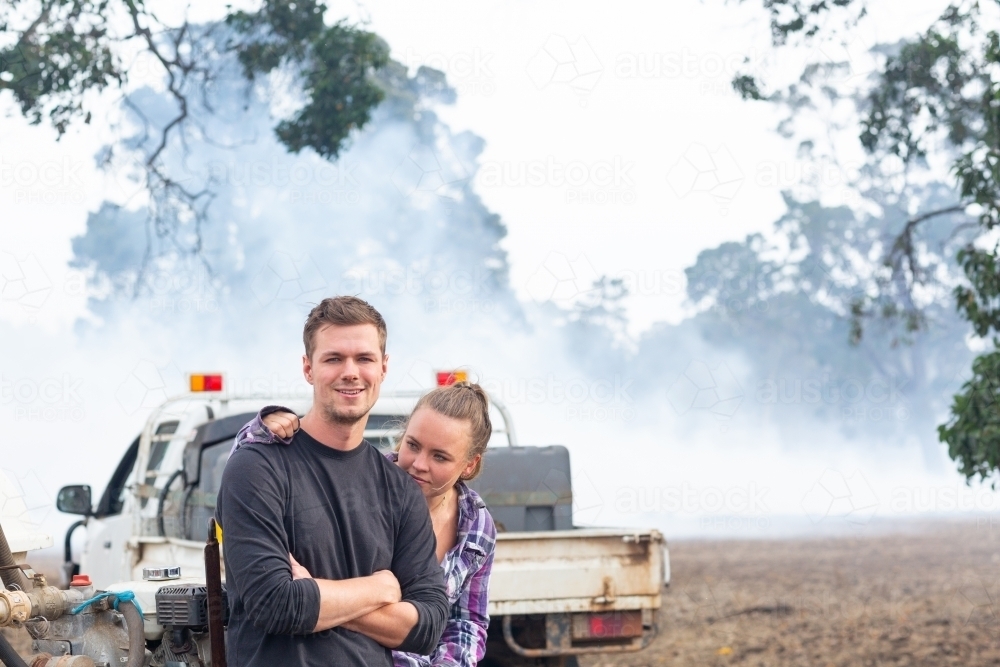 Young couple in front of ute with smoke in background - Australian Stock Image