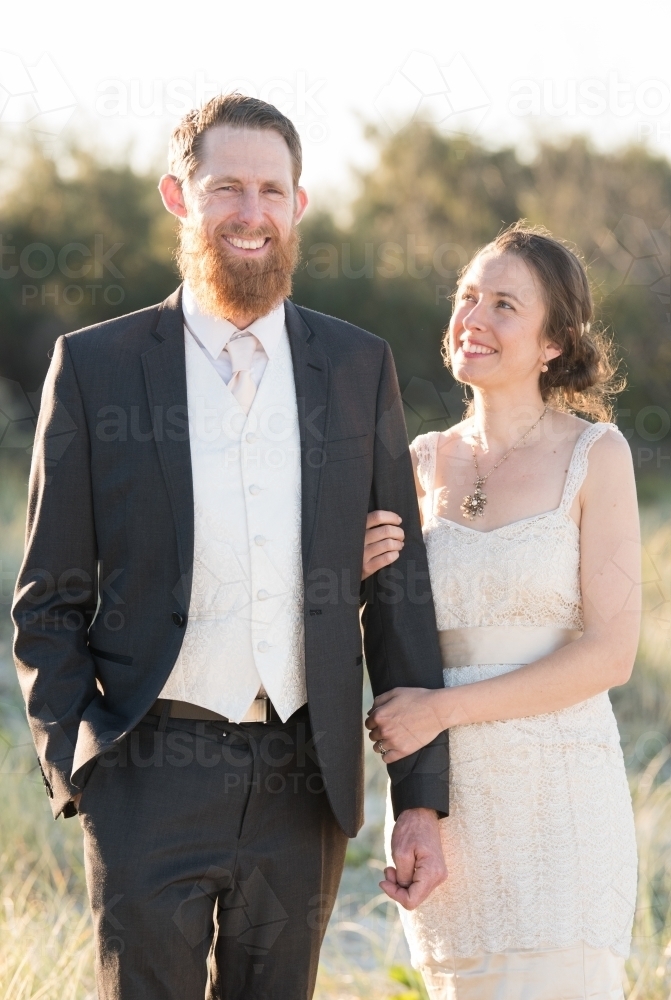 Young couple in portrait pose walk along together among the long grass during golden hour - Australian Stock Image