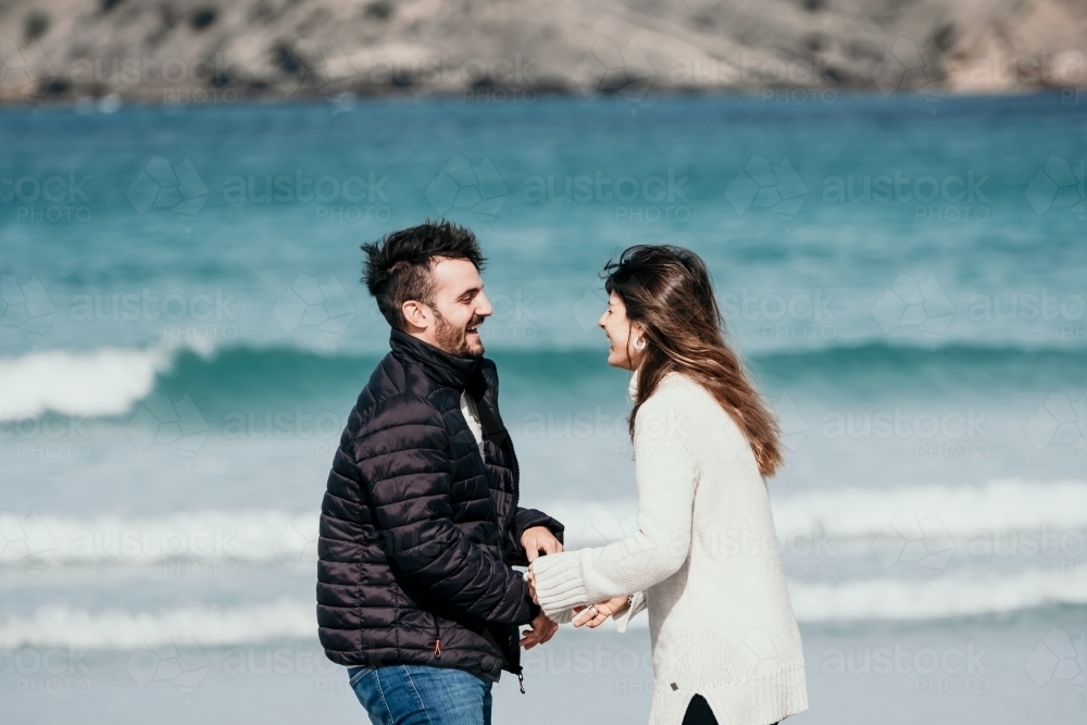 Young couple laughing on the beach in Winter. - Australian Stock Image