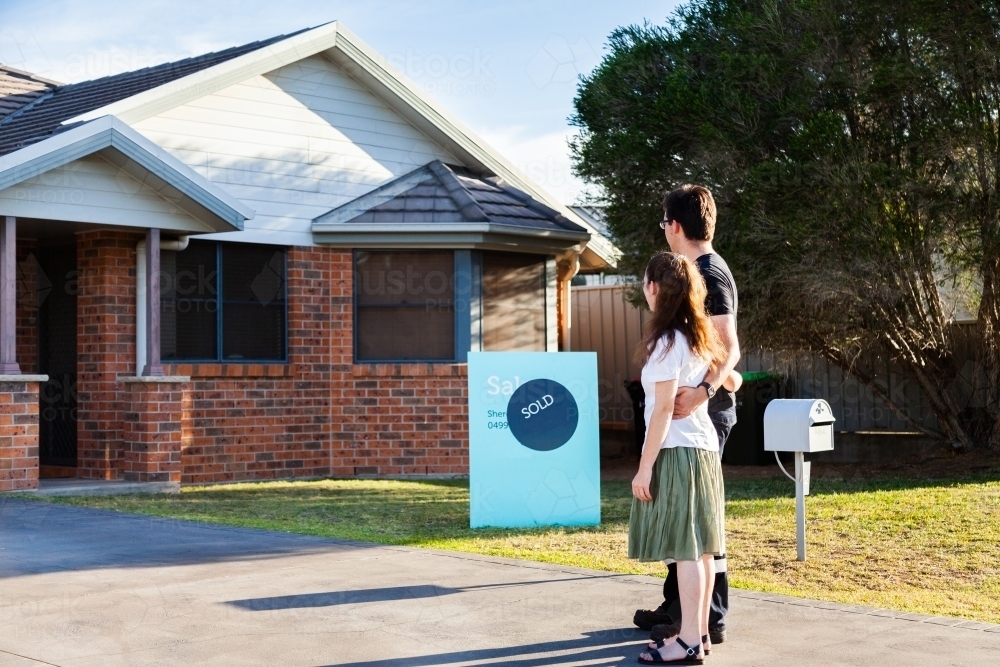 Young couple looking at front of suburban house with sold sign - Australian Stock Image