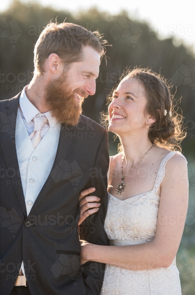 Young couple on wedding day strolling along outdoors in portrait mode. - Australian Stock Image