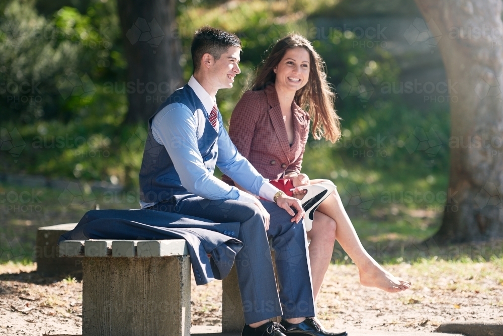 Young couple sitting on a bench in the park talking - Australian Stock Image