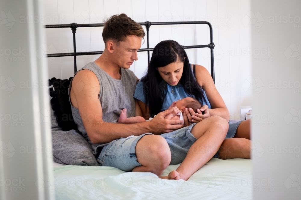 Young couple sitting on bed with new born baby seen from the doorway - Australian Stock Image