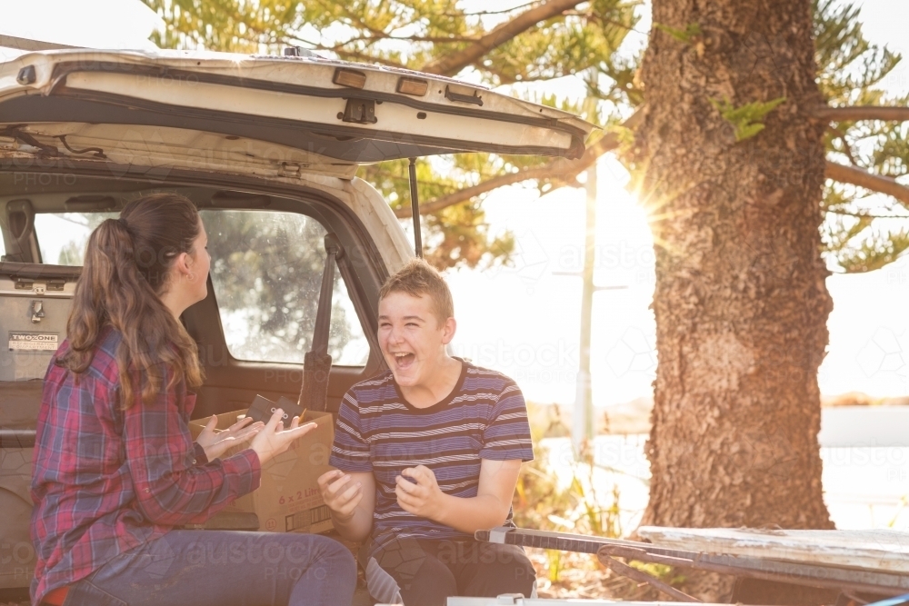 Young couple sitting on tailgate of 4WD vehicle - Australian Stock Image