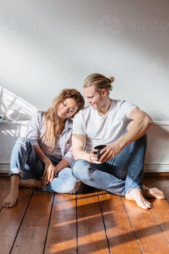 Young couple sitting on the floor relaxing at home : Austockphoto Young couple sitting on the floor relaxing at home - Australian Stock Image