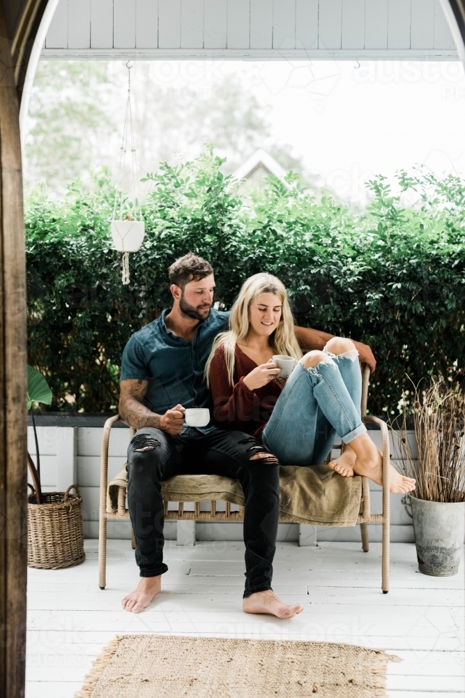 Young couple sitting outside drinking coffee on verandah - Australian Stock Image