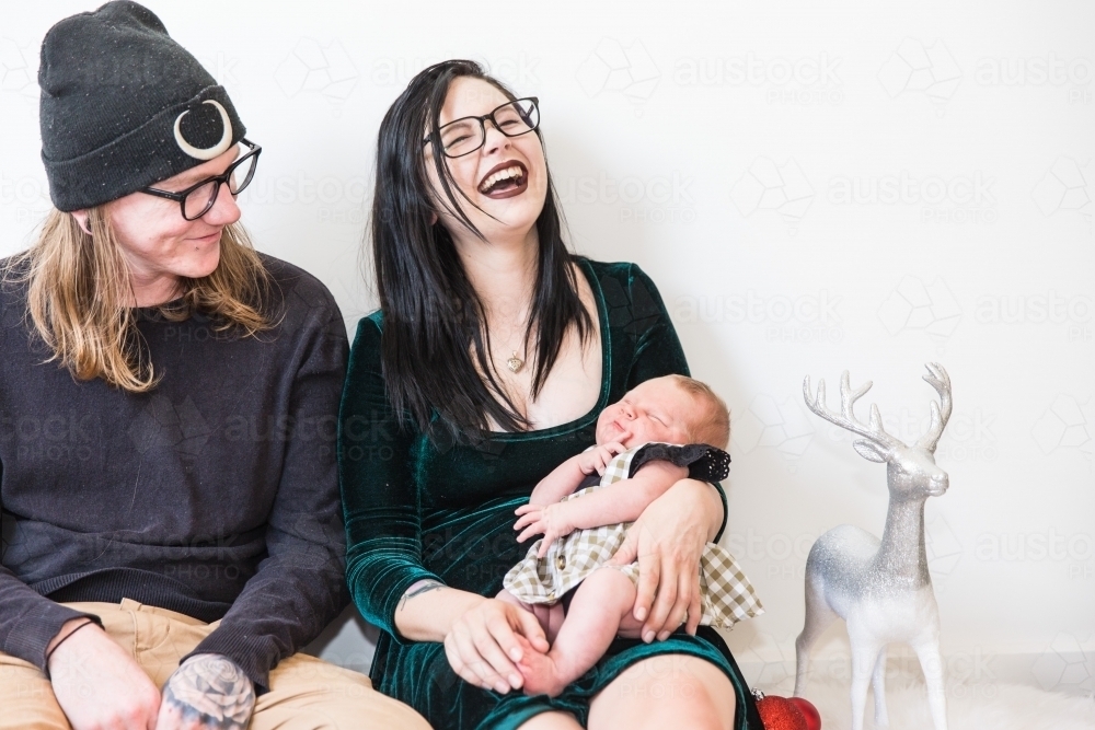 Young couple sitting together mum holding newborn baby head thrown back laughing - Australian Stock Image