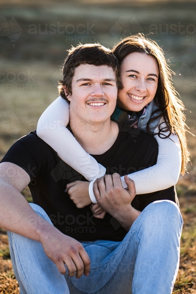 Young couple sitting together smiling with woman's arms wrapped around man - Australian Stock Image