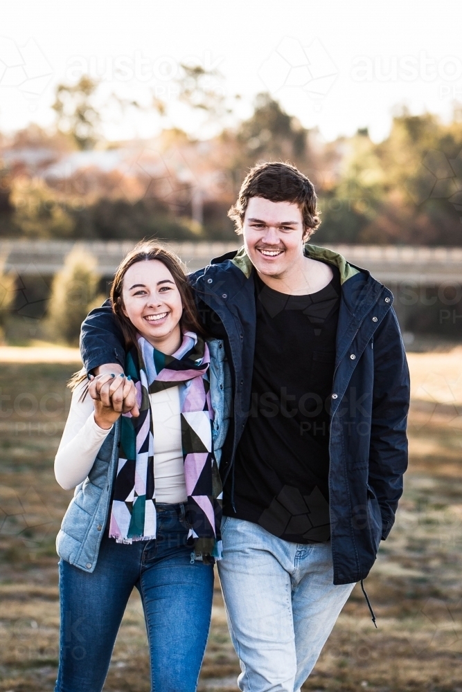 Young couple smiling and holding hands while walking - Australian Stock Image