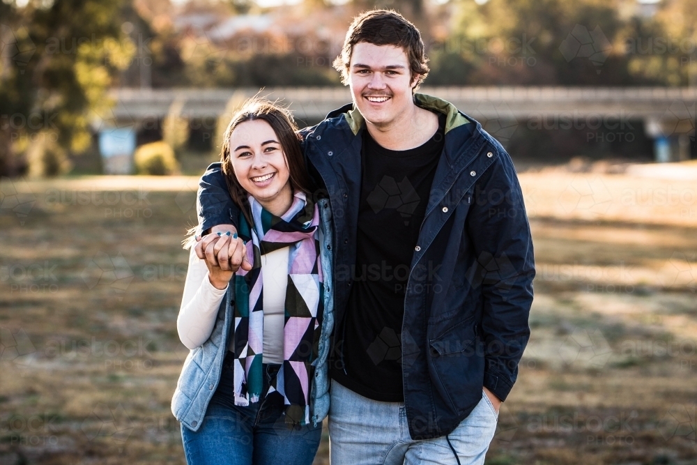 Young couple smiling holding hands walking in park - Australian Stock Image