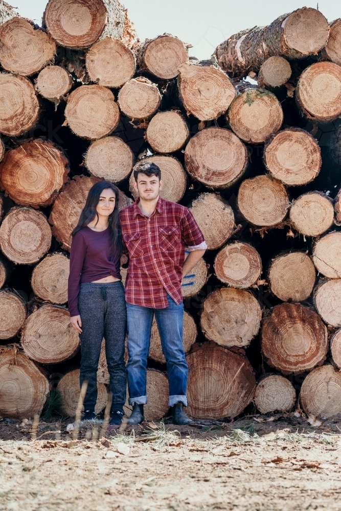 Young couple stand in front of timber pile. - Australian Stock Image