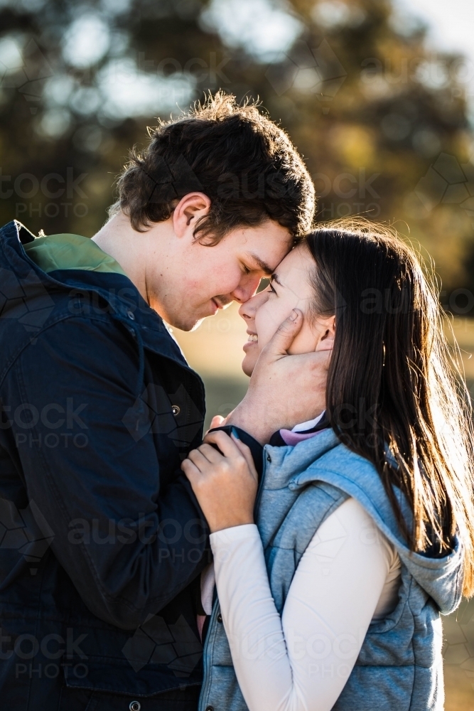 Young couple standing close together foreheads touching him touching her face smiling - Australian Stock Image