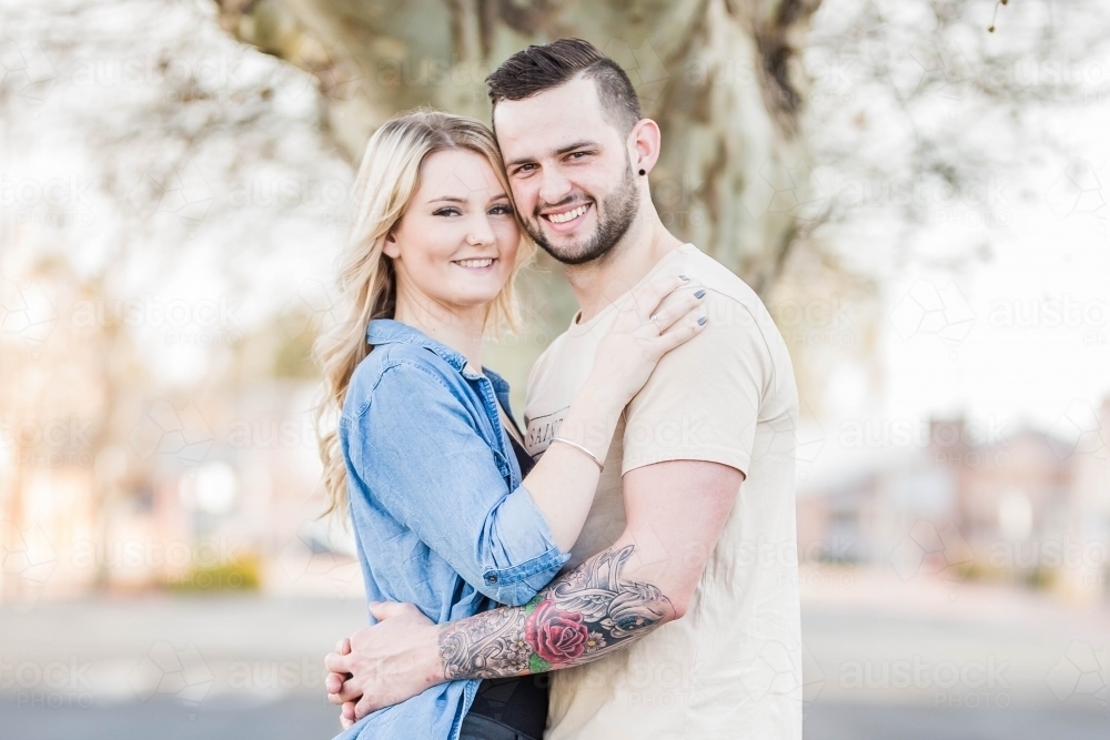 Young couple standing close together with arms around each other - Australian Stock Image